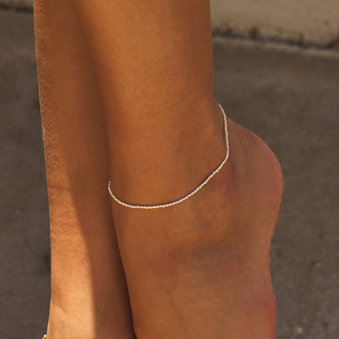 Model wearing dainty pearl anklet with white pearls and 14k gold on one ankle.