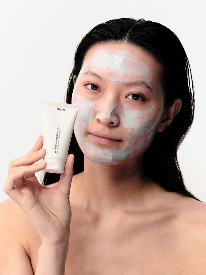 Frau mit Oat Peptide Moisture Mask aufgetragen im Gesicht. Sie hält die Tube in der Hand