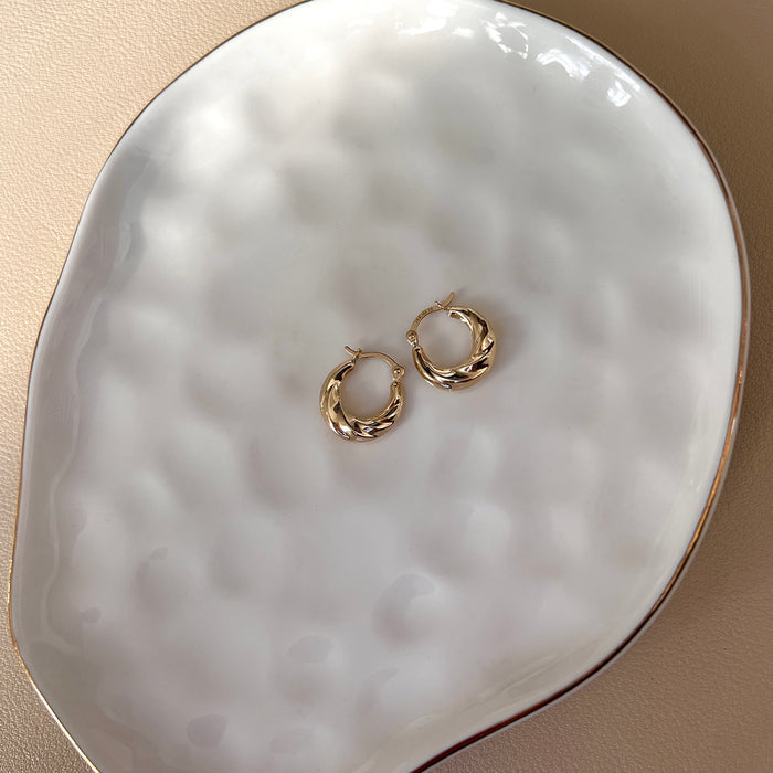 Croissant hoop earrings in 14k yellow gold flat lay on white plate.