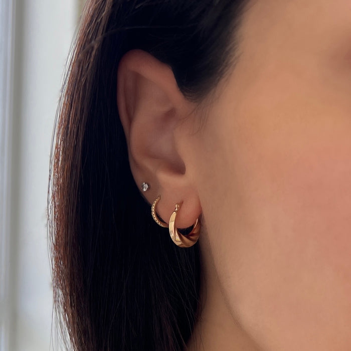 Model wearing croissaint hoop earrings in 14k solid gold on 1st piercing, huggies on 2nd piercing, and diamond stud on 3rd piercing.