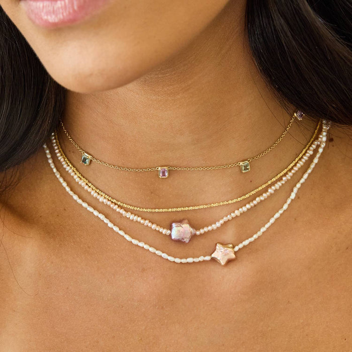 Model wearing four layered 14K solid gold and pearl necklaces. 14 inch station sapphire necklace, a solid yellow gold chain, and two pearl strand necklaces with star shaped pearl pendants.