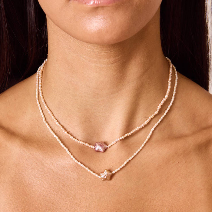 Model wearing two layered necklaces. One 16 inch mini pink freshwater pearl necklace with star pendant and one 18 inch mini white pearl stand with star pendant.