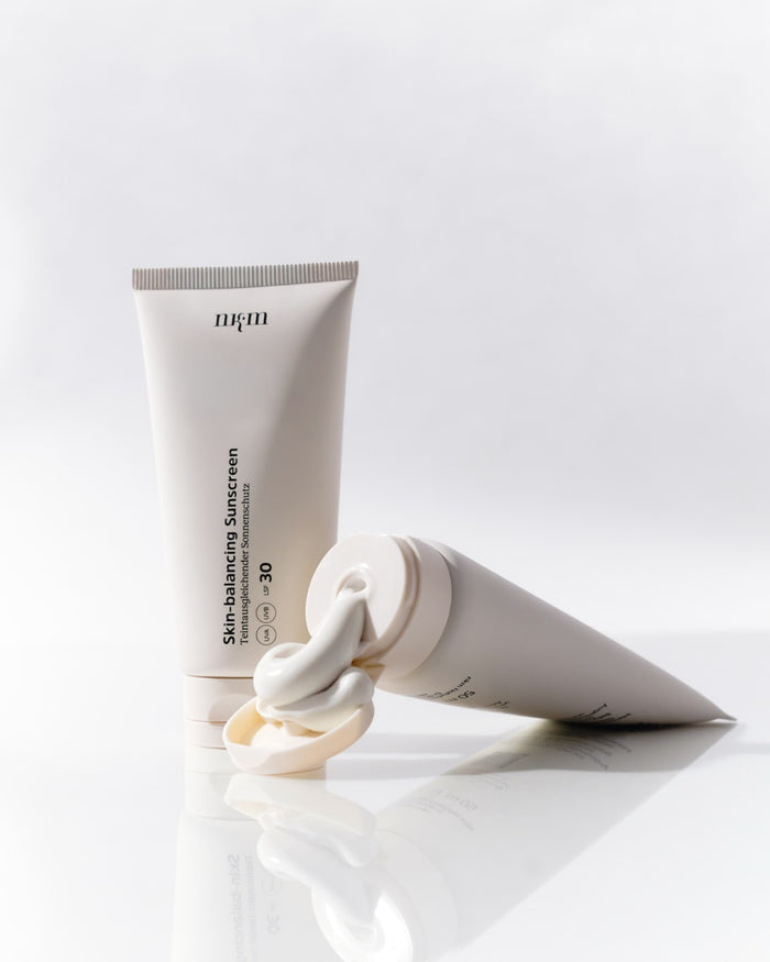 Skin-balancing Sunscreen von nkm. Einmal Tube stehend und einmal Tube liegend mit Konsistenz, die aus der Flasche dgedrückt wird