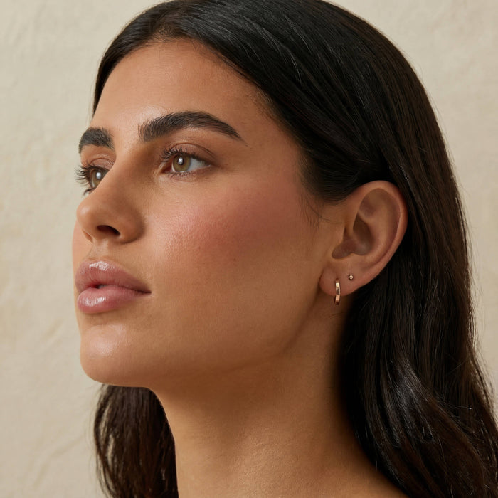 Model wearing 14K solid gold BABYGOLD Everyday Huggie hoop earrings with a ball stud earring in second piercing.